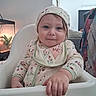 Echo is registered to the contest to win money with this photo: baby, child, high_chair, pajamas, headscarf, bib, smile, indoor, plant, hand, face, curious, seated, clothing, cozy, portrait, young_child, infant, home, furniture