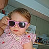 toddler, child, pink_sunglasses, dress, strawberry_pattern, indoor, kitchen, person, face, hair, expression, furniture, appliance, microwave, cupboard, adult, hand, casual, portrait, closeup