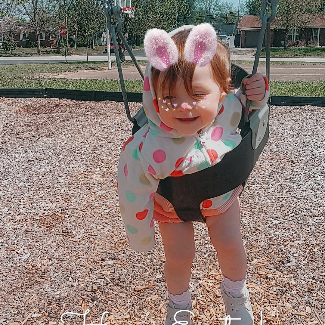 Saroya is registered to the contest to win money with this photo: toddler, child, swing, playground, outdoor, park, smiling, happy, bunny_ears, filter, jacket, polka_dot, shoes, wood_chips, trees, sky, daytime, holiday, text_overlay, easter