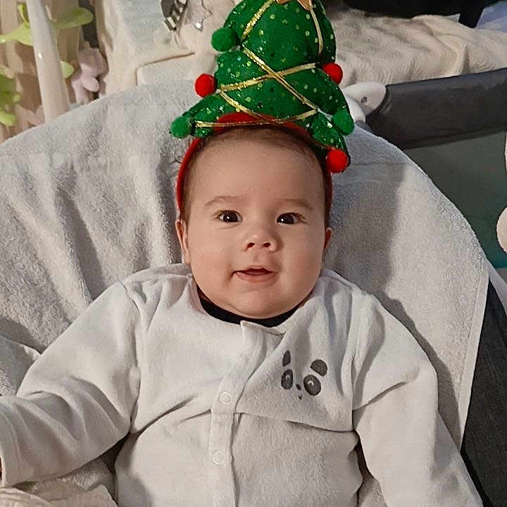 Jalil a rejoint le concours — aidez-le/la à gagner de superbes lots ! baby, celebration, child, christmas_tree_headband, cozy, cute, decor, festive, happy, headwear, holiday, indoors, infant, onesie, panda_design, plush_toy, seated, smiling, snowman, soft_blanket