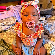 Sevyn is registered to the contest to win money with this photo: baby, child, pacifier, headband, sitting, bed, blanket, car_seat, indoors, cute, portrait, clothing, bracelet, foot, furniture, colorful, person, infant, expression, young_child