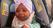 Sevyn joined the competition — help win amazing prizes! baby, baby_girl, bib, car_seat, child, clothing, cozy, cute, flower, hand, happy, headwrap, indoors, infant, pacifier, person, portrait, seatbelt, smile, toy