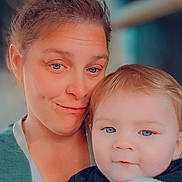Kodi is registered to the contest to win money with this photo: woman, baby, child, person, face, blue_eyes, hair, blanket, holding, indoor, portrait, smile, skin, casual_clothing, head, closeup, family, parent_and_child, human, affection