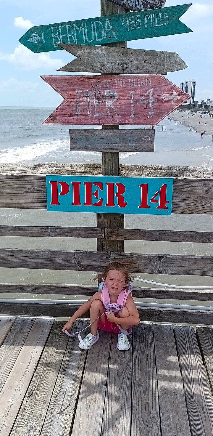 Keelie is registered to the contest to win money with this photo: beach, bench, cloud, coast, font, happy, horizon, leisure, ocean, outdoor_furniture, person, sandal, shore, sitting, sky, summer, t_shirt, toddler, travel, water