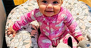 Rebekah is registered to the contest to win money with this photo: baby, child, smiling, pink_onesie, plush_toy, cow_toy, stuffed_animal, cushion, floral_pattern, floor, wooden_floor, indoor, happy, cute, infant, sitting, playpen, toy, person, face