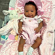 Kelsea is registered to the contest to win money with this photo: baby, infant, pink_outfit, bonnet, smile, blanket, plush_toy, bunny, soft_texture, socks, cute, happy, lying_down, child, indoors, person, comfort, baby_girl, toy, pink