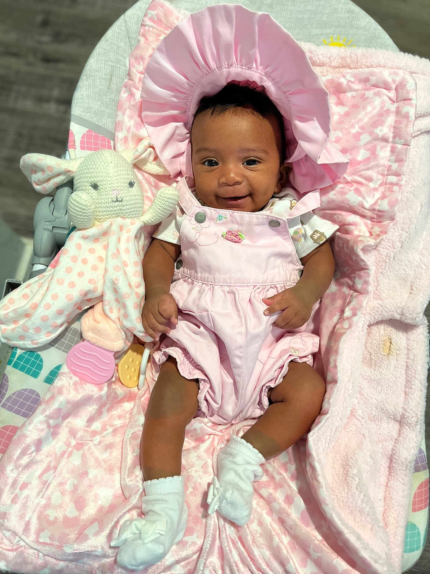 Kelsea is registered to the contest to win money with this photo: baby, infant, pink_outfit, bonnet, smile, blanket, plush_toy, bunny, soft_texture, socks, cute, happy, lying_down, child, indoors, person, comfort, baby_girl, toy, pink