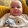 Alfie is registered to the contest to win money with this photo: baby, infant, pacifier, cushion, yellow, striped_clothing, koala_design, closeup, indoor, hand, face, cheeks, cute, child, portrait, soft_lighting, expression, seated, cozy, young