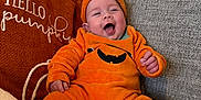 Alfie is registered to the contest to win money with this photo: baby, child, couch, cozy, cute, fabric, happy, headwear, home, indoor, laughing, orange, person, pillow, plush, portrait, pumpkin_costume, seated, smiling, soft_lighting
