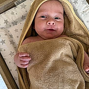 Alfie is registered to the contest to win money with this photo: baby, towel, hood, infant, face, skin, hand, blanket, bed, changing_pad, star_pattern, wood, furniture, cute, child, young, wrapped, portrait, indoors, smiling