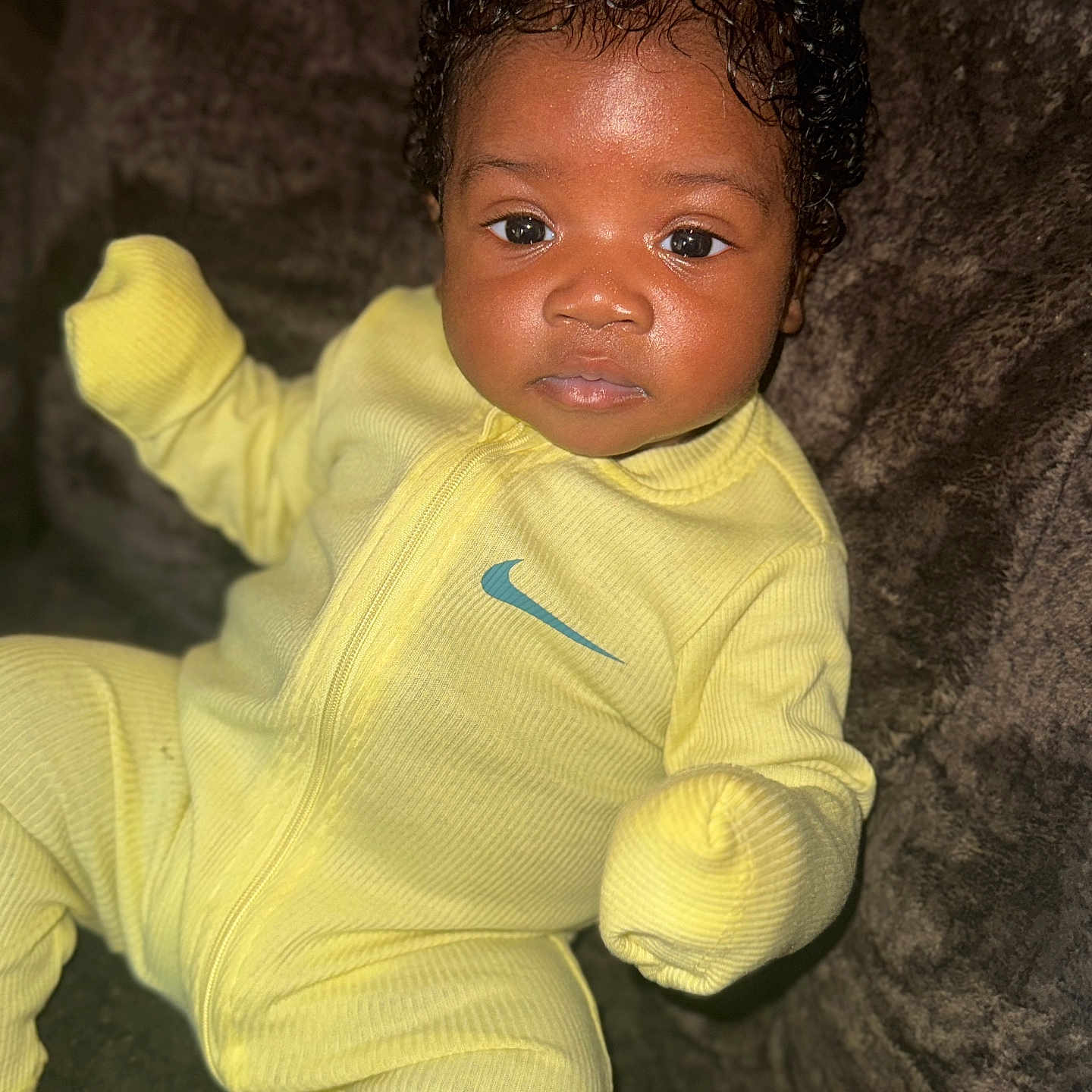 Jaikhyius joined the competition — help win amazing prizes! baby, brown_background, child, clothing, comfortable, cozy, curly_hair, cute, eyes, face, indoors, infant, looking_at_camera, nike_logo, portrait, sitting, soft_texture, warm, yellow_onesie, young_child