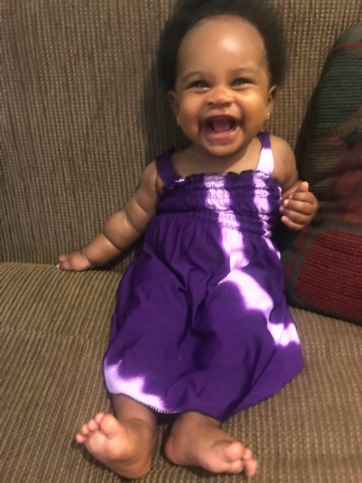 Zola is registered to the contest to win money with this photo: arm, baby, cheek, child, dress, face, facial_expression, finger, fun, gesture, happy, head, person, purple, skin, smile, thumb, toddler