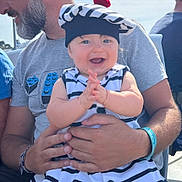 Mélyne participe au concours pour gagner de l'argent avec cette photo : baby, child, man, smiling, clapping, striped_clothing, beret, red_pom_pom, outdoor, daylight, happy, person, holding, facial_expression, beard, short_sleeves, seated, casual_wear, blue_eyes, hands