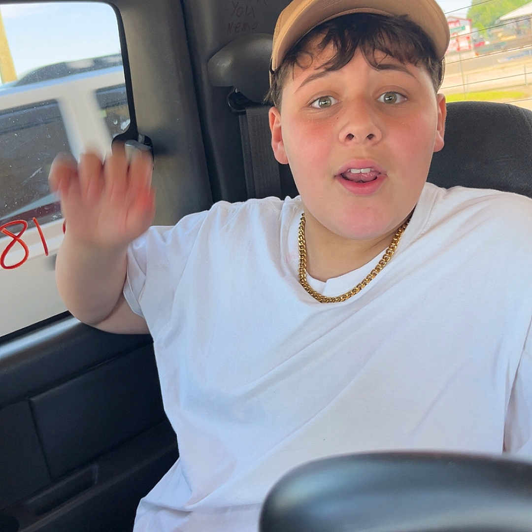 Jacob joined the competition — help win amazing prizes! background, boy, cap, car_seat, casual_clothing, chain, child, daytime, expression, face, gesture, person, road, seat, seatbelt, sunlight, transport, vehicle_interior, white_tshirt, window