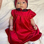 Anahi is registered to the contest to win money with this photo: baby, infant, red_dress, headband, plaid, white_socks, bow, blanket, soft_texture, lying_down, portrait, cute, child, young, face, hands, footwear, cozy, indoor, fashion