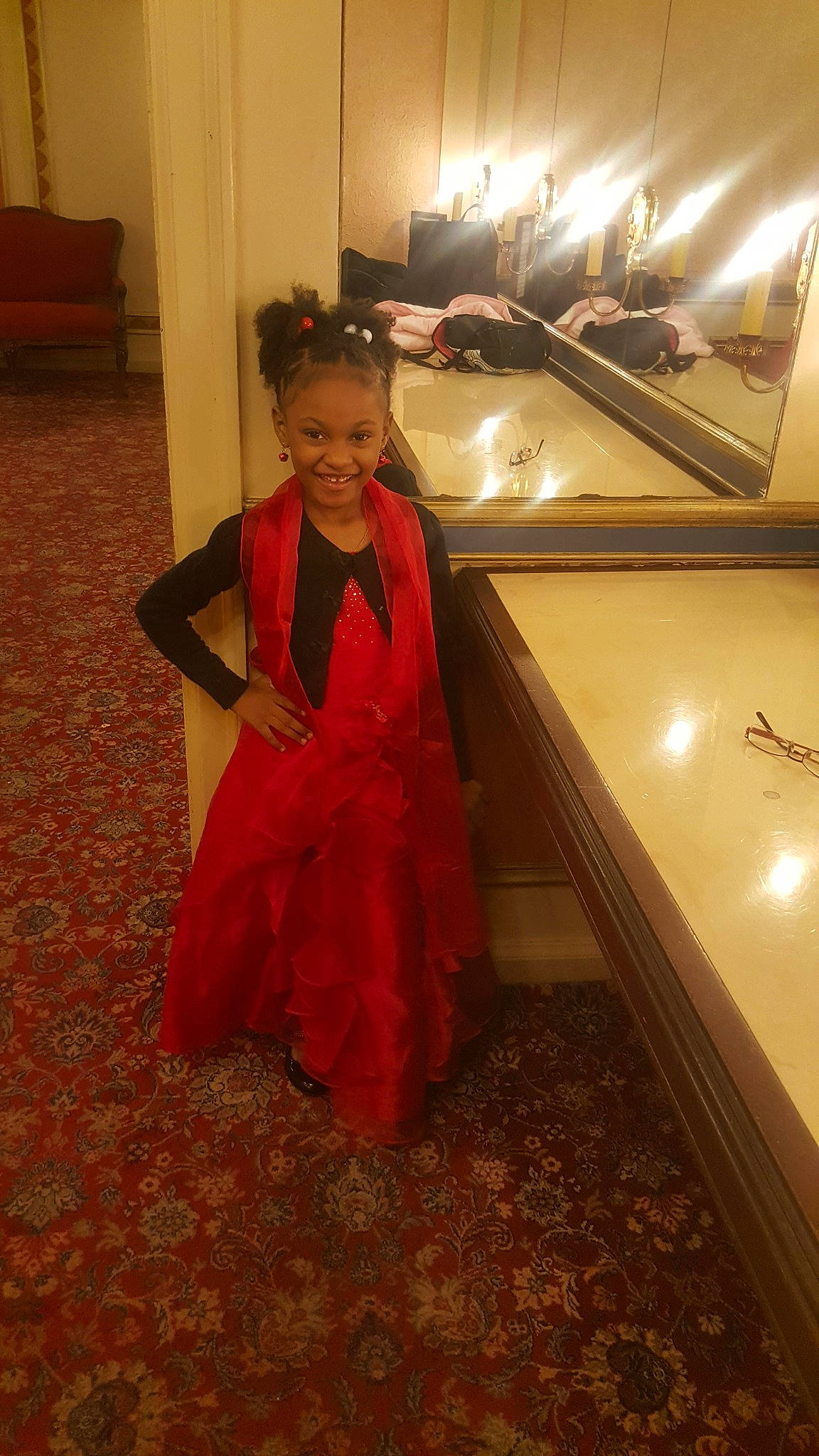 D'Ari is registered to the contest to win money with this photo: child, clothing, costume, day, dress, floor, flooring, formal_wear, fun, girl, gown, joy, lady, outerwear, person, red, room, skin, smile, standing