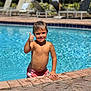 background, blue, boy, child, daytime, happy, holiday, lounge_chair, outdoor, pool, recreation, skin, smile, summer, sunny, swim_trunks, swimming, thumbs_up, water, wet_hair