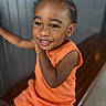 child, toddler, smile, orange_clothing, bench, happy, portrait, indoors, face, cute, person, short_hair, skin, young, sitting, joyful, expression, bright, background, casual