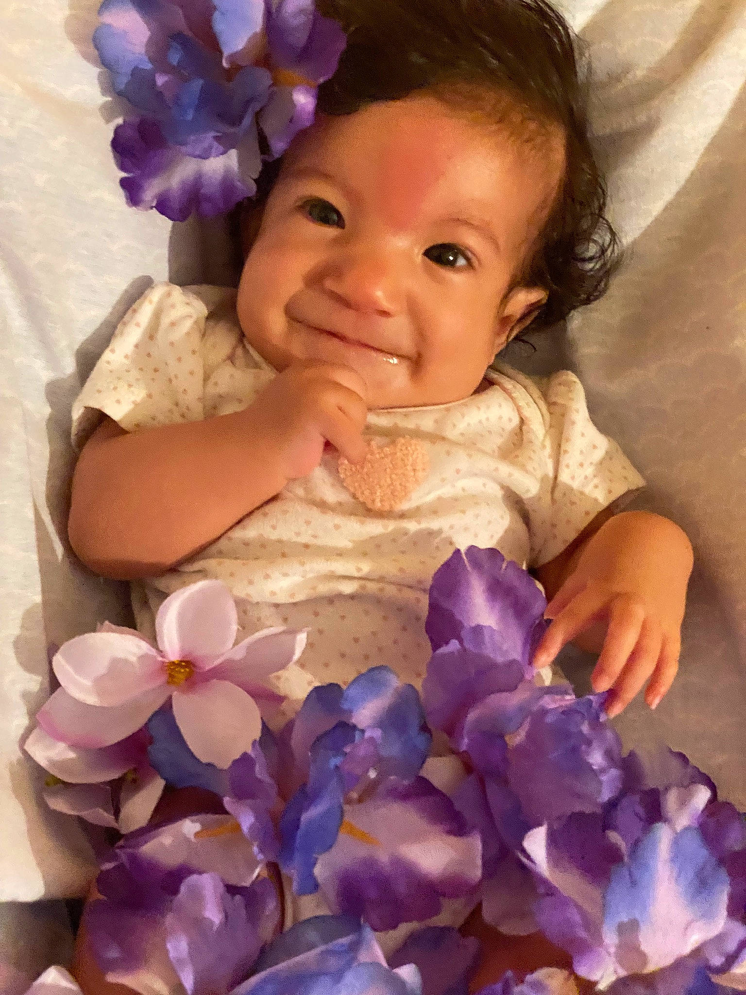 Carla is registered to the contest to win money with this photo: arm, baby_toddler_clothing, blue, clothing, dress, finger, flower, gesture, hand, happy, human_body, iris, joy, organ, person, petal, pink, plant, purple, smile