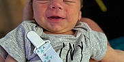 Micah is registered to the contest to win money with this photo: baby, infant, smile, onesie, pacifier_clip, person, face, sleeping, hand, lap, skin, clothing, young_child, resting, indoor, cute, peaceful, newborn, human, blurred_background