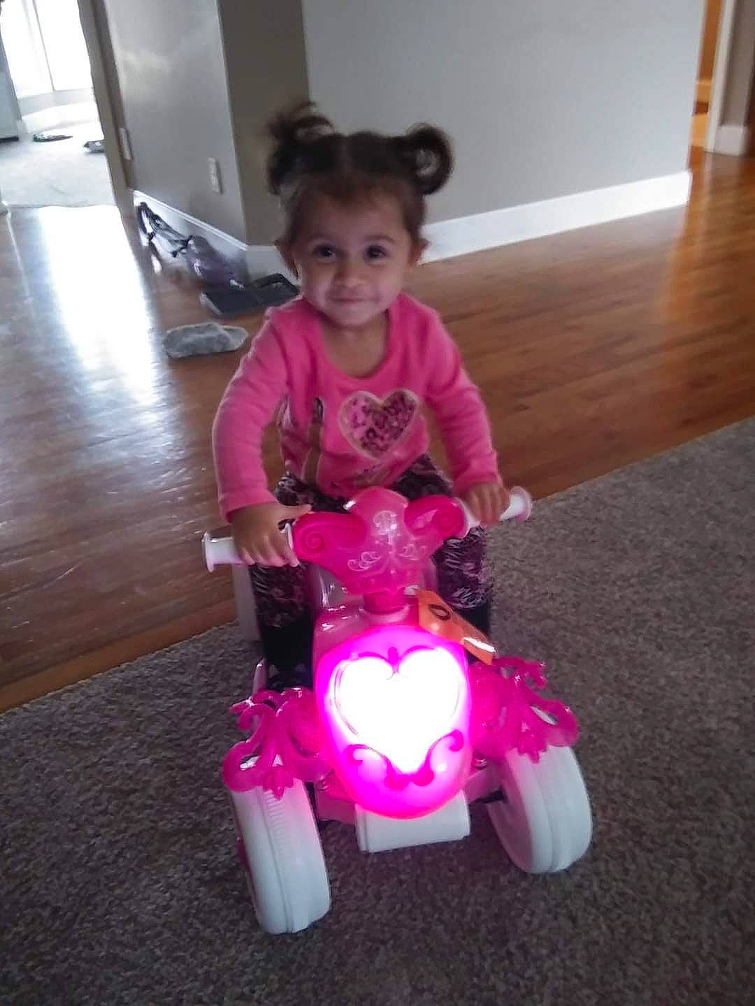 Jurnee is registered to the contest to win money with this photo: automotive_wheel_system, carmine, child, event, floor, flooring, fun, hardwood, joy, magenta, person, pink, purple, riding_toy, sitting, smile, tire, toddler, toy, toy_vehicle