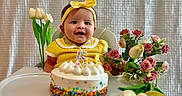 Isabella is registered to the contest to win money with this photo: baby, birthday_cake, celebration, child, decor, flowers, food, happy, headband, high_chair, indoor, number_candle, person, portrait, roses, smiling, table, tulips, white_tights, yellow_clothing