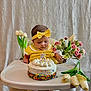 baby, birthday, cake, candle, celebration, child, cute, festive, flowers, headband, high_chair, indoor, pink_flowers, sitting, sprinkles, table, toddler, white_background, white_tulips, yellow_clothing