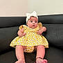 baby, child, infant, yellow_dress, headband, bow, black_couch, indoors, cute, chubby_cheeks, barefoot, sitting, young_child, furniture, portrait, person, skin, expression, curious, comfortable