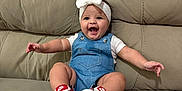 Isabella joined the competition — help win amazing prizes! arms_outstretched, baby, bow, child, comfortable, couch, cute, denim_overalls, footwear, happy, headband, indoor, infant, nike_shoes, person, portrait, sitting, smiling, white_shirt, young_child