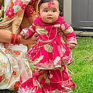 Anaya joined the competition — help win amazing prizes! baby, child, traditional_clothing, pink_dress, grass, outdoor, person, face, holding_hands, red_mark, jewelry, earrings, adult, saree, floral_pattern, garden, door, celebration, festive, smiling
