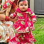 baby, child, traditional_clothing, pink_dress, grass, outdoor, person, face, holding_hands, red_mark, jewelry, earrings, adult, saree, floral_pattern, garden, door, celebration, festive, smiling