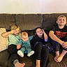 child, baby, couch, sofa, living_room, pillow, striped_pajamas, black_pants, tshirt, barefoot, smiling, playing, sitting, indoor, family, siblings, happy, relaxing, kids, casual