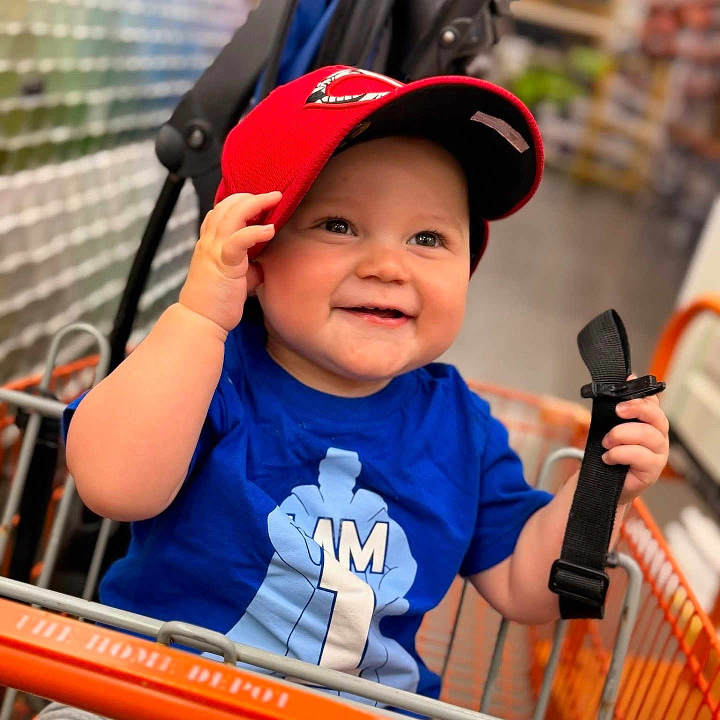 Giovanni is registered to the contest to win money with this photo: toddler, child, shopping_cart, red_cap, blue_shirt, smiling, holding, store, aisle, blurred_background, happy, baby, person, clothing, indoor, retail, seat, hand, cute, casual
