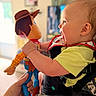 Giovanni is registered to the contest to win money with this photo: baby, child, toy, woody, doll, smile, happy, indoor, person, playful, yellow_shirt, bib, hand, face, profile, infant, closeup, holding, excitement, fun