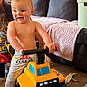 Giovanni is registered to the contest to win money with this photo: toddler, child, toy_truck, yellow, indoor, living_room, beard, adult, smile, shirtless, carpet, blanket, couch, play, happy, person, handlebar, pants, window_light, furniture