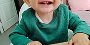 Tyler a rejoint le concours — aidez-le/la à gagner de superbes lots ! toddler, child, smiling, happy, face, hands, green_sweater, table, indoor, living_room, pink_couch, pillow, wood, person, cute, teeth, short_hair, portrait, young_child, home