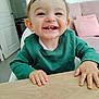 toddler, child, smiling, happy, face, hands, green_sweater, table, indoor, living_room, pink_couch, pillow, wood, person, cute, teeth, short_hair, portrait, young_child, home