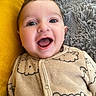 baby, infant, smiling, happy, face, eyes, onesie, clothing, bear_pattern, blanket, fur_texture, yellow_cushion, cozy, cute, child, portrait, indoor, soft_texture, closeup, person