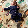 baby, infant, blue_clothing, knitwear, play_mat, animal_print, forest_theme, hedgehog, bear, deer, owl, mushroom, leaf, child, cute, lying_down, indoor, soft_texture, colorful, curious