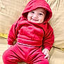baby, child, smile, red_hoodie, red_pants, couch, beige_couch, indoors, happy, cute, infant, clothing, sitting, portrait, face, hood, person, young_child, cozy, casual