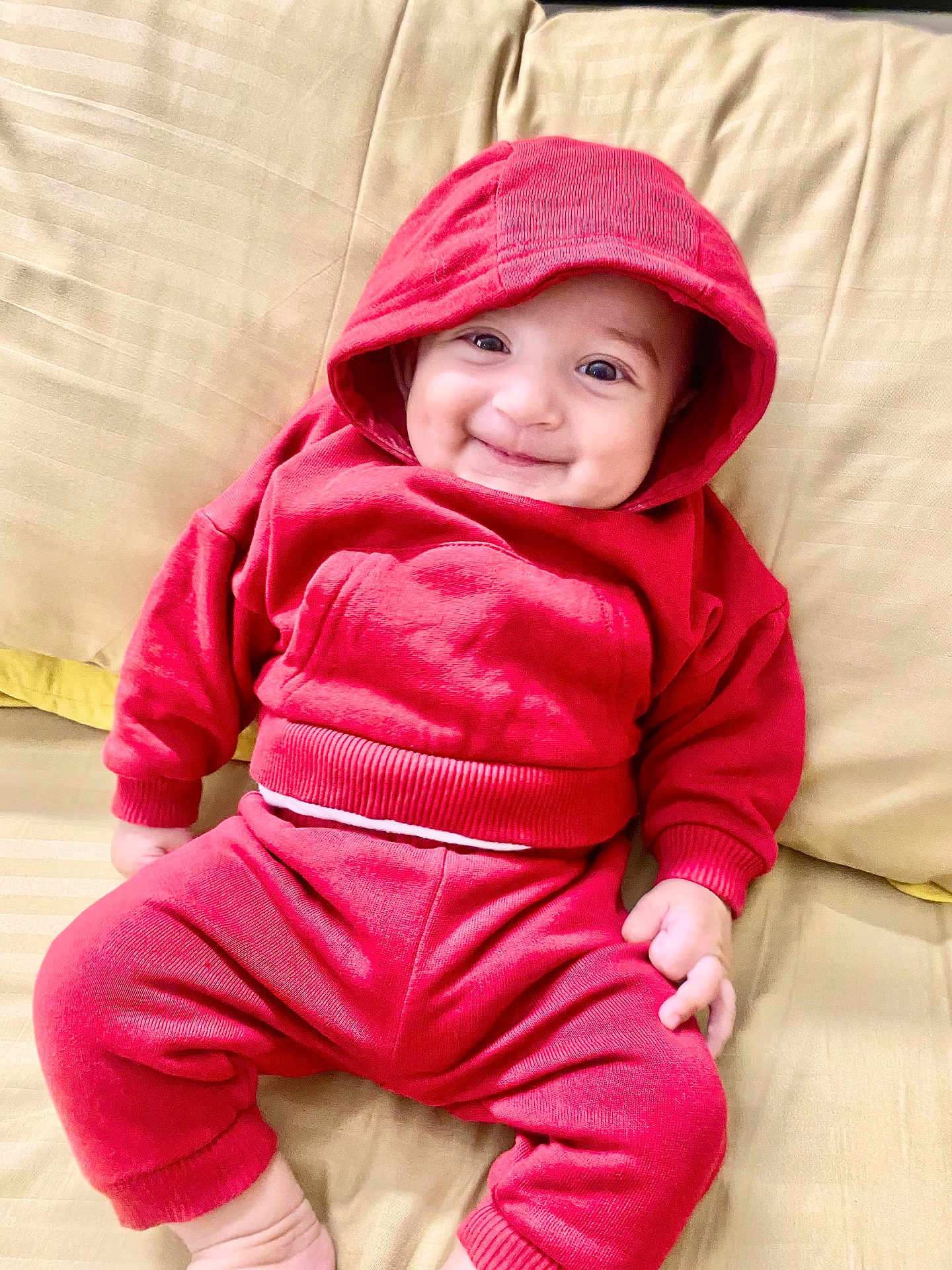 Nofal joined the competition — help win amazing prizes! baby, child, smile, red_hoodie, red_pants, couch, beige_couch, indoors, happy, cute, infant, clothing, sitting, portrait, face, hood, person, young_child, cozy, casual