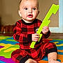 baby, child, indoor, pajamas, red_clothing, checkered_pattern, foam_mat, colorful, playtime, sitting, curious, hands, feet, toy, bright_colors, expression, face, floor, home, infant