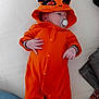 baby, infant, orange_onesie, hood, pacifier, bed, blanket, sleepwear, cute, child, newborn, lying_down, soft_fabric, indoor, clothing, comfort, resting, small_hands, face, sleepy