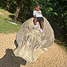 Jonnesty joined the competition — help win amazing prizes! child, elephant, statue, outdoor, park, jungle, forest, nature, sitting, portrait, braids, beads, smiling, clothing, shorts, shoes, stone, sculpture, sunlight, gravel