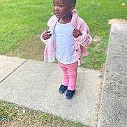 Jonnesty is registered to the contest to win money with this photo: child, toddler, girl, portrait, outdoor, park, sidewalk, grass, pink_jacket, pink_pants, white_shirt, boots, standing, fashion, curly_hair, smiling, looking_away, daylight, blurred_background, street_scene