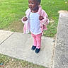child, toddler, girl, portrait, outdoor, park, sidewalk, grass, pink_jacket, pink_pants, white_shirt, boots, standing, fashion, curly_hair, smiling, looking_away, daylight, blurred_background, street_scene