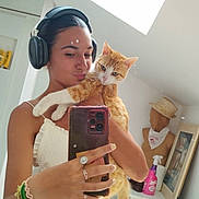 Winnie participe au concours pour gagner de l'argent avec cette photo : woman, cat, selfie, mirror, headphones, smartphone, orange_cat, white_cat, indoor, casual_clothing, bracelets, rings, mannequin, hat, bandana, skylight, toilet, spray_bottle, mirror_reflection, bedroom