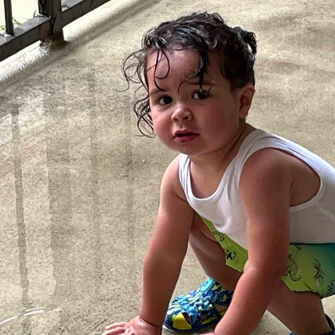 Adam joined the competition — help win amazing prizes! toddler, child, wet_hair, curly_hair, splashing_water, concrete_floor, colorful_shoes, shorts, white_tank_top, outdoor, balcony, railing, hands, crouching, expression, casual_clothing, summer, playful, young_child, person