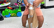 Adam joined the competition — help win amazing prizes! toddler, child, toy_horse, toy, indoor, store, floor, shelf, clothing, shorts, polo_shirt, footwear, curly_hair, play, plastic_toy, looking_away, white_shoes, floor_tiles, retail, shopping_aisle