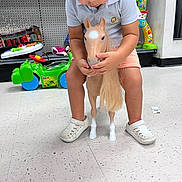 Adam joined the competition — help win amazing prizes! child, toddler, toy_horse, toy_store, floor, white_shoes, shorts, polo_shirt, plastic_toy, green_toy, indoor, playing, curly_hair, looking_down, colorful, sitting, hands, face, feet, casual_clothing